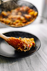 woman puts food from a frying pan into a plate