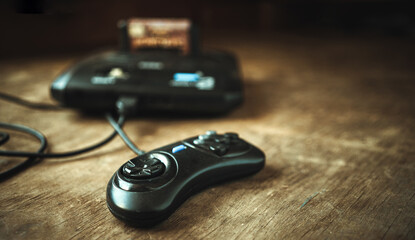A TV game console from the 90s. A black joystick and a set-top box with cartridges on a wooden table in retro style.