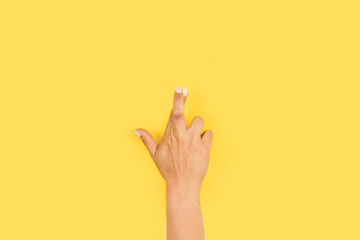 Mano de mujer con los dedos cruzados sobre un fondo amarillo liso y aislado. Vista de frente y de cerca. Copy space - obrazy, fototapety, plakaty