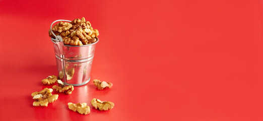 A small metal bucket filled with walnuts on a red background. Concept of healthy eating.