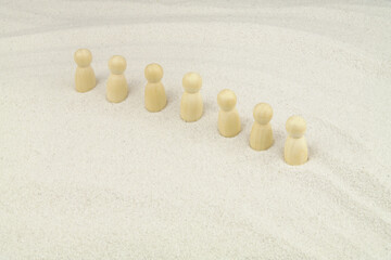 Fototapeta na wymiar Wooden people figures in row on white sand background. Caravan concept. 