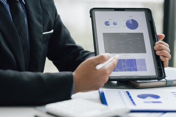 Businessman analyzes company marketing growth data and makes investment plans on tablet. Sales strategy analysis and business investment planning.