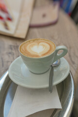 Eine Tasse Cappuccino mit einem Herz aus Milchschaum auf silbernen Tablett.