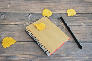 notepad isolated on wooden background with dry birch leaves and black pen