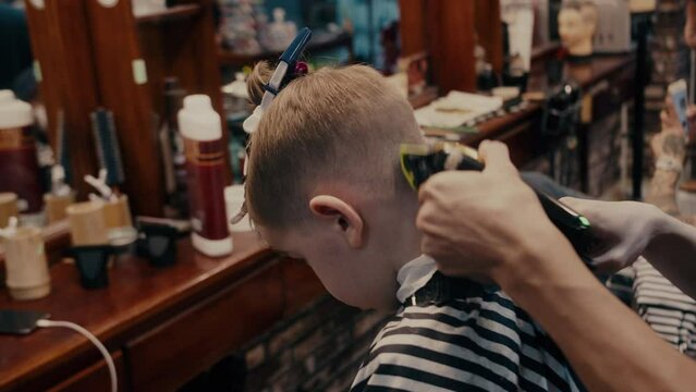 Fashionable hairdresser cuts a child's hair with a clipper in a barbershop. Close up side view portrait Men's hairstyle and haircut in the salon.