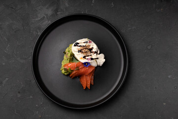 Appetizer with cheese, avocado and salmon on a black plate