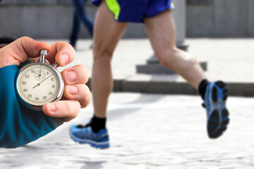 measuring the running speed of an athlete using a mechanical stopwatch. hand with a stopwatch on the background of the legs of a runner