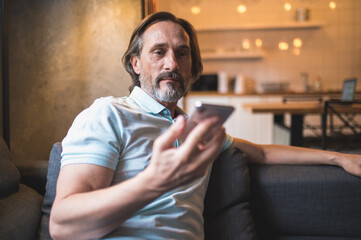 Bearded man sitting in the armchair awith a smartphone in hand