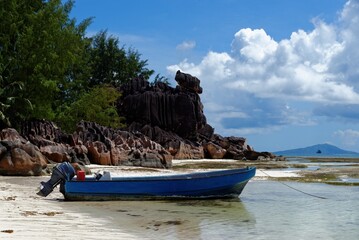 Motor boat at the beach on Curieuse Island, Seychelles, with lava stone rocks and lush vegetation