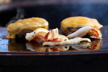 Fried bacon with two burgers with cheese in the soft focus in background.