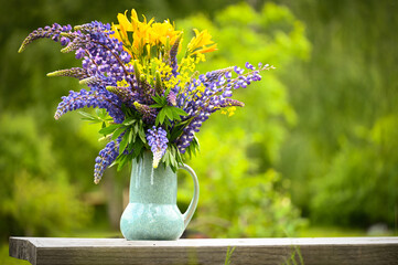 beautiful summer bouquet of wild flowers in a vase. yellow lilies and blue lupins on a green...