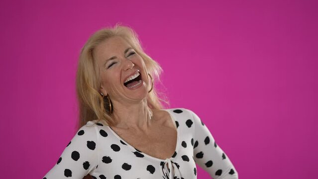 Portrait of fashionable laughing happy beautiful mature woman isolated on solid pink background.