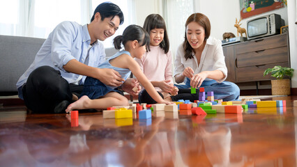 Asian family with children playing and building tower of colorful wooden toy blocks in living room...