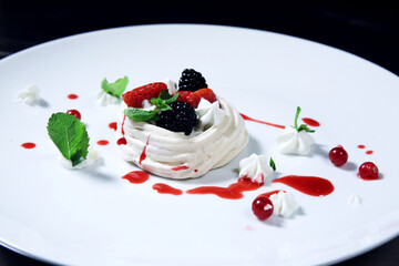 Meringue cake Pavlova with fresh strawberry and blackberry on a white plate. Side view.