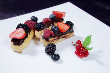 Eclairs with custard, berries, raspberry and strawberries. Eclairs with glaze and strawberries on a white plate.