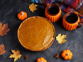 pumpkin pie and two cups of hot tea or coffee in orange sweatshirts on the table with a knitted scarf, autumn leaves and pumpkins. top view