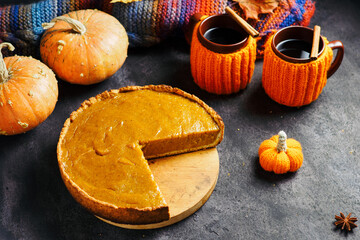pumpkin pie and two cups of hot tea or coffee in orange sweatshirts on the table with a knitted scarf, autumn leaves and pumpkins. top view