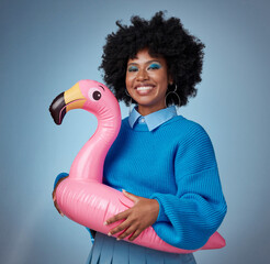 Portrait of woman in blue with a flamingo and a smile on her face. Happy black woman with inflatable bird rubber ring on hip on blue background. Mockup for trendy, travel and fun for summer vacation © N Felix/peopleimages.com
