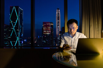 Man working with laptop and cellphone at night