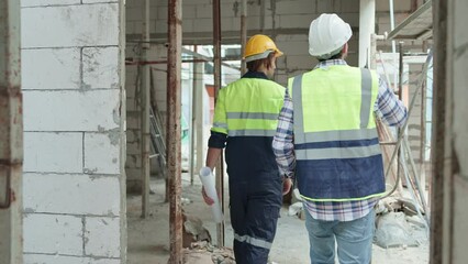 Two professional male civil engineer or Architect, inspector with contractor, foreman or worker. While walk looking inspect discuss meeting building project on construction site.