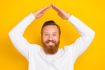 Portrait of positive cheerful man arms showing roof gesture above head isolated on yellow color background