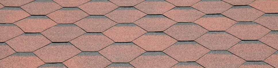Reddish and faded surface. View of bituminous or composite shingles on the roof of a building. Figured roof using decorative material of artificial origin. Patterned irregular texture