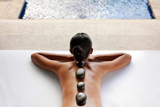 Woman receiving Hot Stone Massage in the gazebo of a private pool villa at a spa resort. Bali, Indonesia