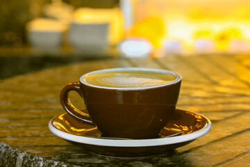 Brown ceramic cappuccino cup, freshly brewed coffee with milk on a wooden table. Beautifully decorated caffeine drink. Serving a warm autumnal season beverage in cafe, restaurant. Latte art concept.
