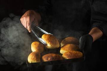 Oven baked buns on a hot baking sheet in the chef hand in glove. The cook takes a hot bun with a...