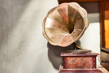 Vintage photo of old dust covered phonograph on wooden cabinet and white wall.