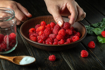 Chef prepares compote or fruit drink with raspberries. The cook hand while sorting and cleaning in the kitchen.