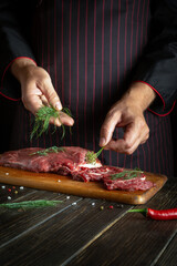 The chef putting dill leaves on meat before grilling. Space for recipe or hotel menu on dark background