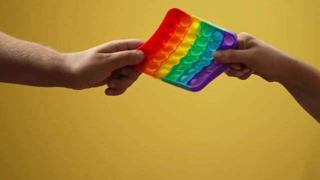 Hand of unrecognizable woman winning in colorful fidget toy competing with man. Close-up male and female palms pulling stretching multicolored sensory toy leaving in slow motion at yellow background