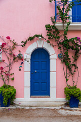 Fototapeta na wymiar Traditional greek house with colorful blue door and pink walls at Asos village. Assos peninsula famous and extremely popular travel destination in Cephalonia, Greece, Europe