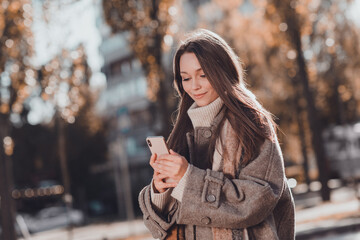 Photo of optimistic long brown hairdo lady hold telephone wear coat sweater outside in park - obrazy, fototapety, plakaty
