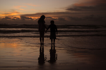 Silhouette portrait of lovely sibling on the beach shore at sunset having fun time.