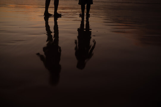 Silhouette reflection of sibling playing on the beach during beautiful sunset.