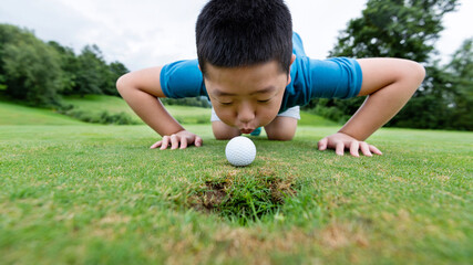 Little boy blowing golf ball into hole