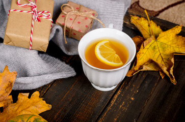 Autumn mood concept. Hot tea with lemon and leaves on wooden background