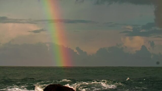 A rainbow in the sky with clouds after a storm over a rough sea. Long shot taken with a tripod