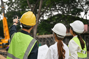 Back view image with Asian young foreman and engineer checking the construction project with commitment to success at construction site.