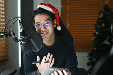 Portrait with The Asian radio host man wear Santa hat speaking in microphone while moderating a...