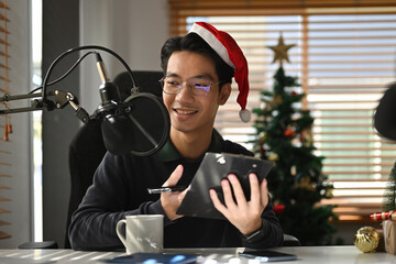 Smiling and gesturing radio host man speaking with microphone and laptop, holding program on air,...