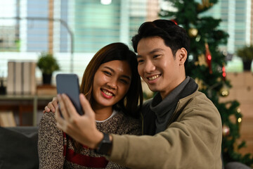 Young Asian man using smartphone taking a selfie with his girlfriend on the Christmas Day.