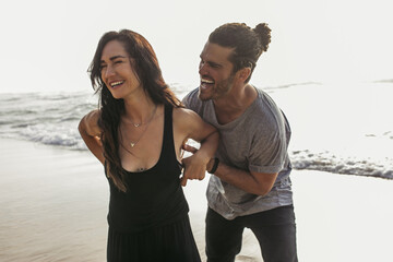 cheerful man tickling smiling girlfriend in dress near ocean in portugal.