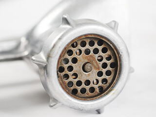 A gray manual metal retro meat grinder with a rusty mesh with round holes on a marble table.