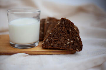 Cut black bread into pieces on a wooden cutting board next to a glass of fresh milk.