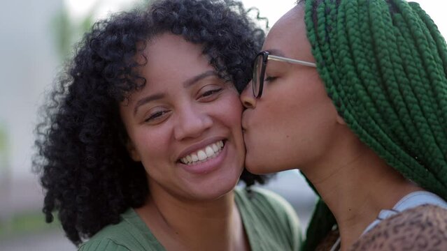 Two black sisters showing love and affection. African American sibling kissing friend in cheek. Happy Hispanic South American people fanuky care