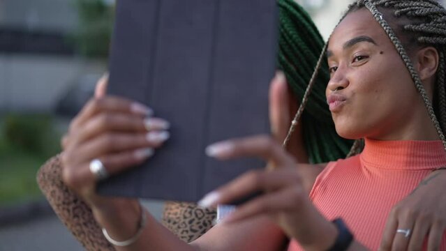 Two young black women taking selfie with tablet. African American girlfriends with braided hairstyle holding device outdoors