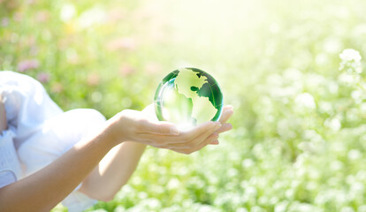 Earth Day or World Environment Day, environmentally friendly concept. Save our planet, restore and protect green nature, sustainable lifestyle and climate literacy theme. Crystal glass globe in hands.